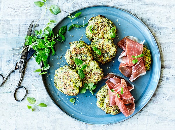 En tallerken med quinoa-frikadeller, skiver af skinke og friske krydderurter