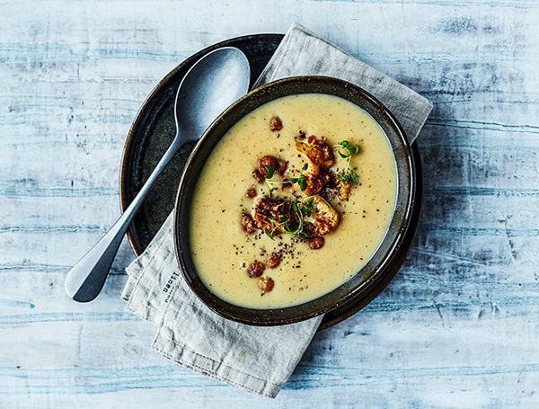 En skål kartoffelsuppe med baconstykker og krydderurter på toppen.