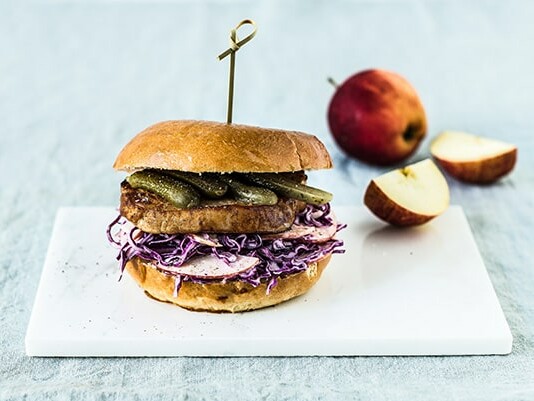 Bøfsandwich med rødkål og skiver af æble på skærebræt med æble i baggrunden