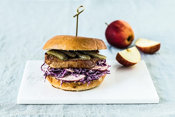 Bøfsandwich med rødkål og skiver af æble på skærebræt med æble i baggrunden