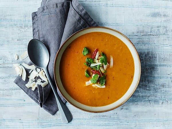 En skål suppe dekoreret med kokosflager og friske urter