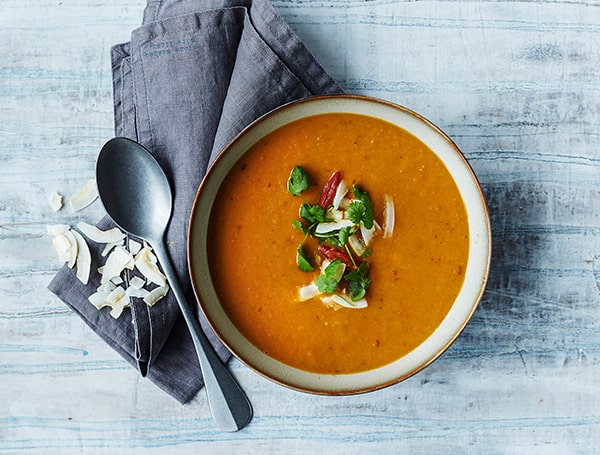 En skål suppe dekoreret med kokosflager og friske urter