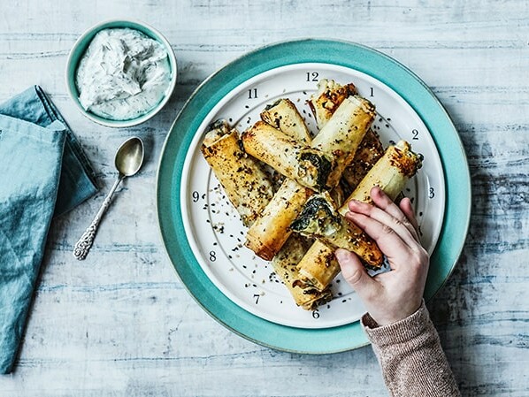 En hånd rækker ud efter en tallerken fyldt med sprøde madpandekager ved siden af en skål dip. ---