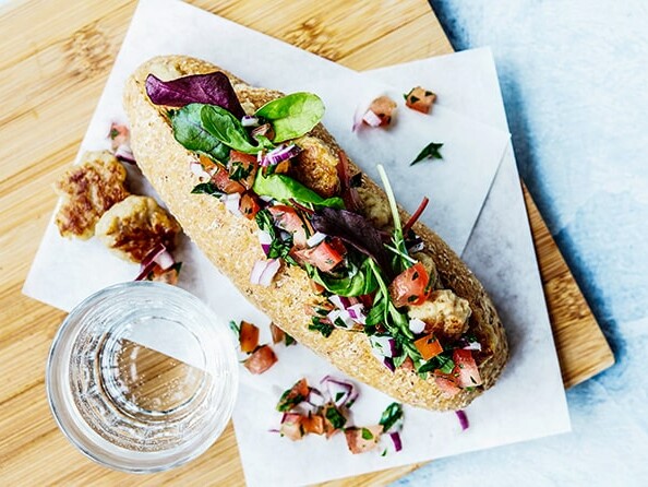 Sandwich med grønne blade, tomater og løg serveret på et bræt