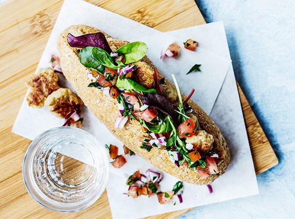 Sandwich med grønne blade, tomater og løg serveret på et bræt