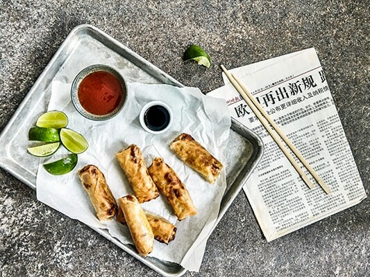 Forårsruller på en bakke med sauce, lime og aviser