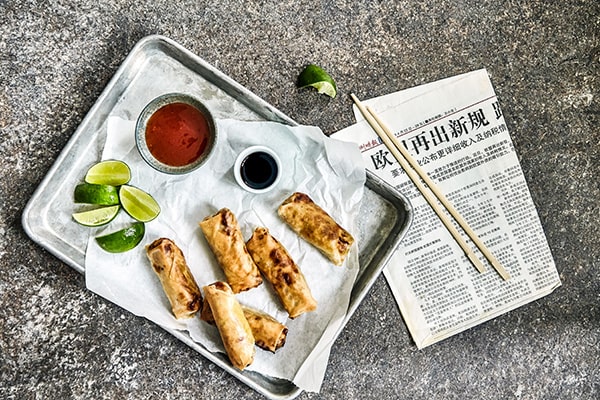 Forårsruller på en bakke med sauce, lime og aviser