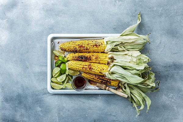 Grillede majskolber med lime og sauce på et fad