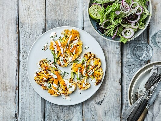 Grillede blomkålsskiver med dressing ved siden af salat og glas