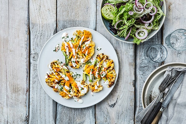 Grillede blomkålsskiver med dressing ved siden af salat og glas