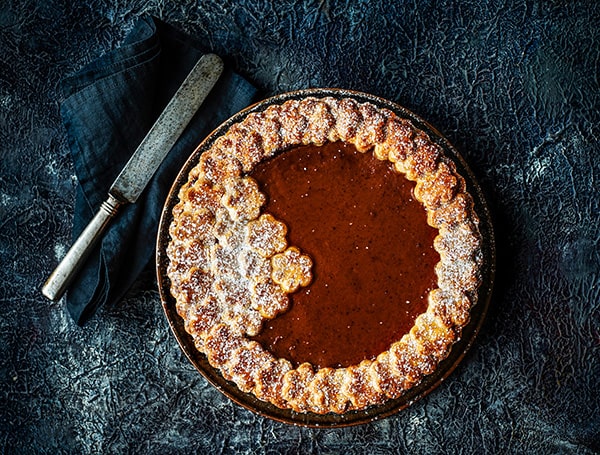 Elegant chokoladetærte med dekoreret blomsterkant og rustikt bestik