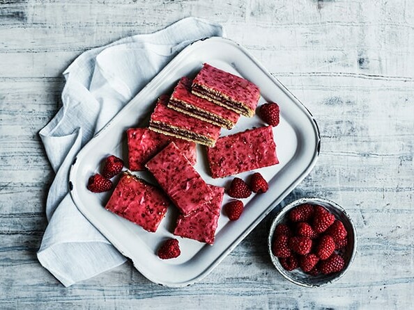 Et hvidt fad med hindbærsnitter og friske hindbær.