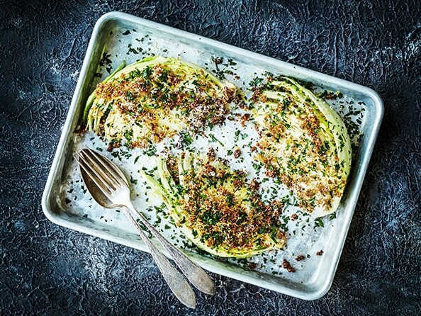 Grillet spidskål på plade drysset med krydderurter og brødkrummer, med gaffel og ske ved siden af.