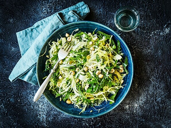 En grøn salat i en blå skål med nødder og gaffel