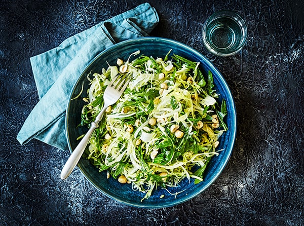 En grøn salat i en blå skål med nødder og gaffel