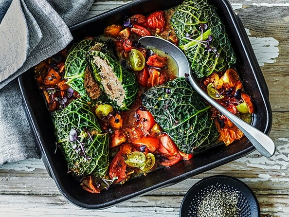 Bagte kålblade fyldt med fars og friske grøntsager i en sort bageform