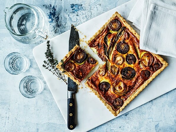 Hjemmelavet løgtærte på et marmorbræt med glas og kniv