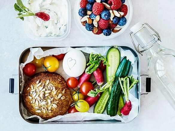 En frokostboks fyldt med grøntsager, æg, og en skål bær ved siden af