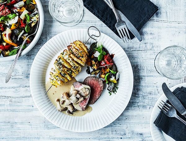 Tallerken med skiver af kartoffel, kød og grøntsager.