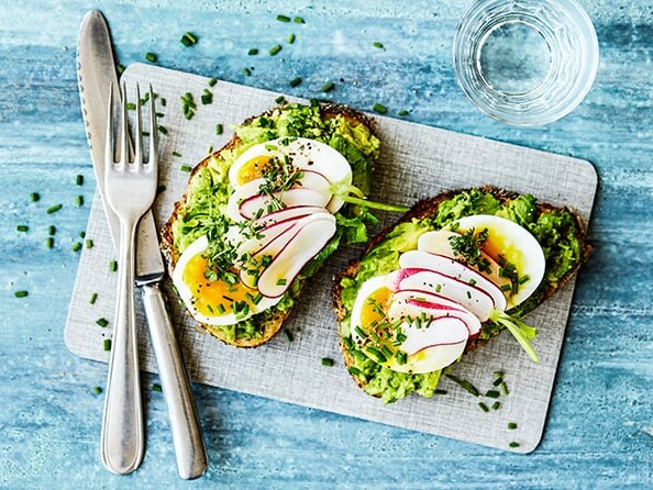 To skiver brød med avocado, æg og radiser på skærebræt