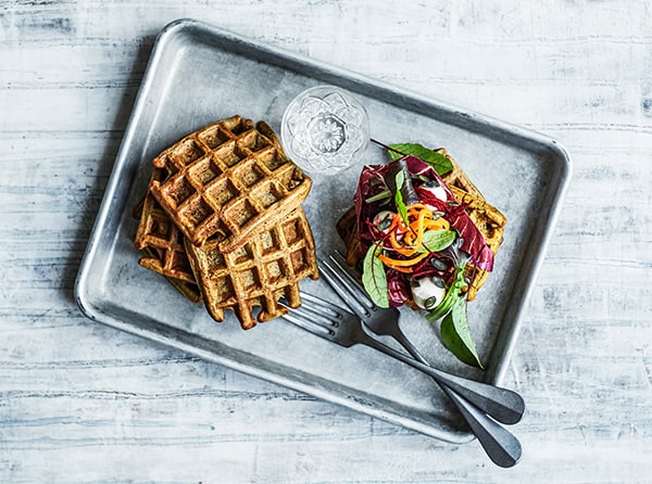Vafler med farverig salat og glas vand på metalbakke
