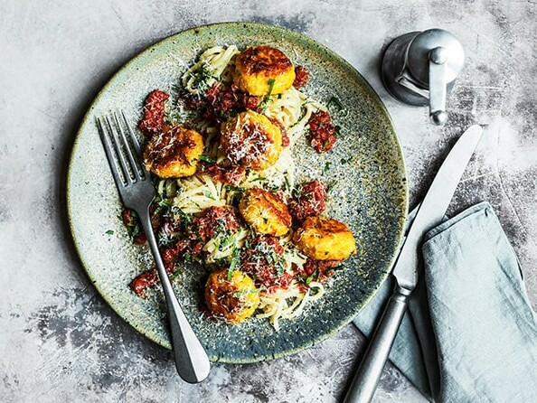 Tallerken med spaghetti, kødboller og tomatsauce, serveret med bestik.