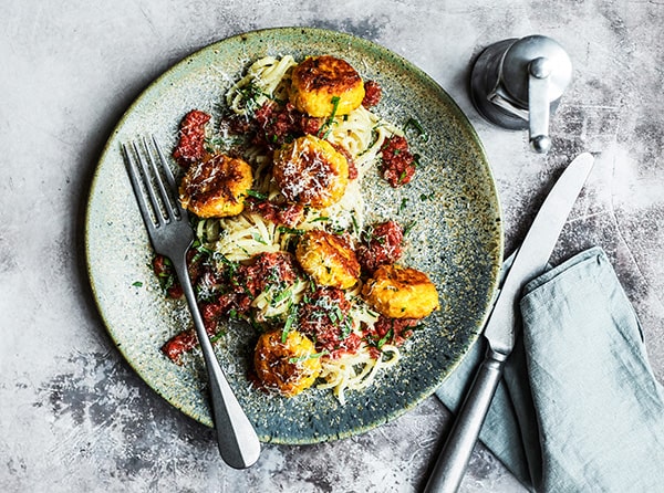 Tallerken med spaghetti, kødboller og tomatsauce, serveret med bestik.