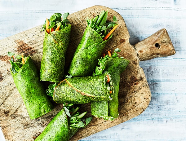 Friske grønne wraps fyldt med grøntsager på et rustikt skærebræt