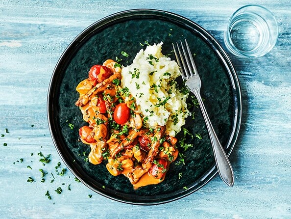 Sort tallerken med oksegryde og kartoffelmos, pyntet med urter og stilfuldt anrettet