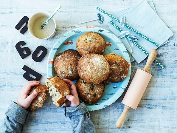 En tallerken med friskbagte boller, sugerør og et barn der bryder en bolle i to.