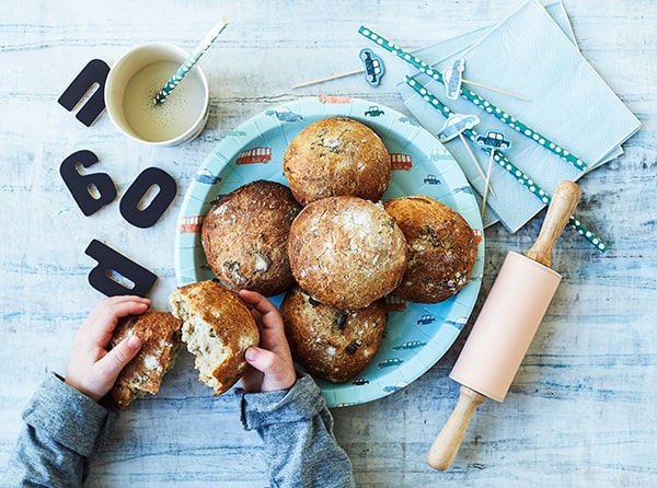 En tallerken med friskbagte boller, sugerør og et barn der bryder en bolle i to.