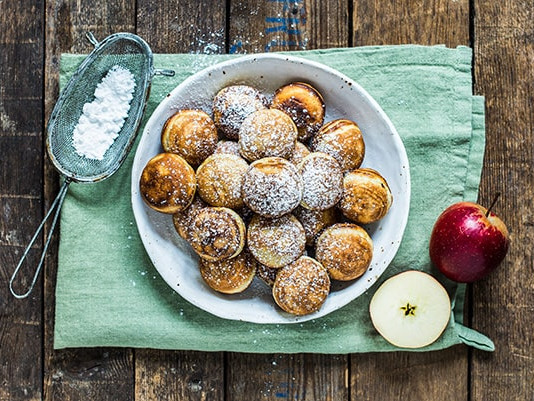 Hvid tallerken med æbleskiver og flormelis på rustikt træbord med æble og grønt klæde