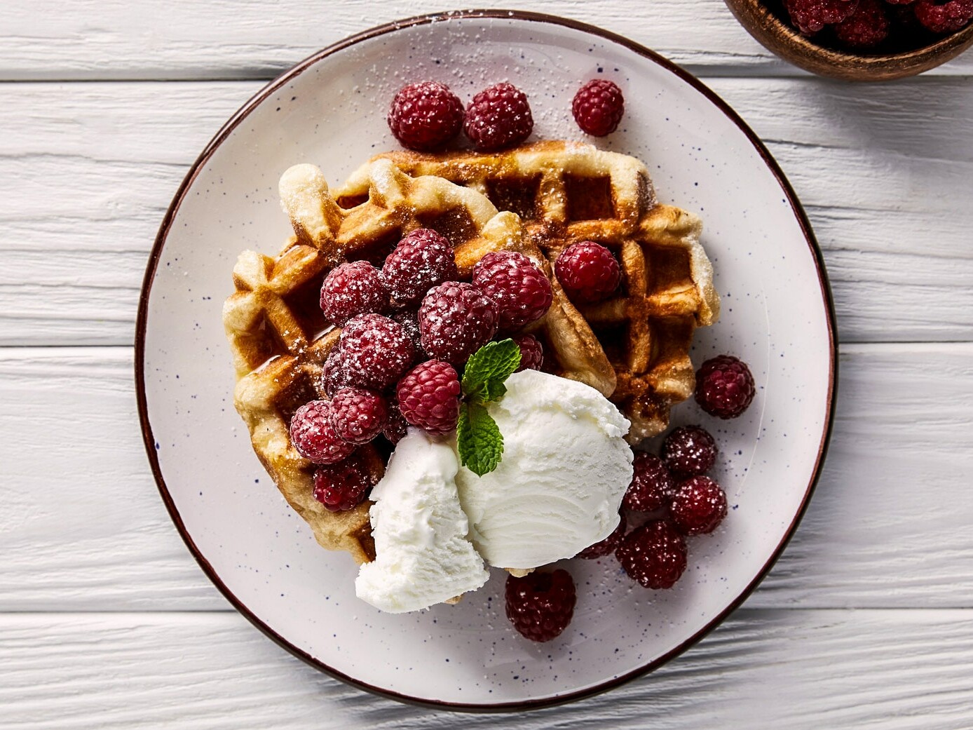 En tallerken med belgiske vafler toppet med hindbær og kugle vaniljeis.