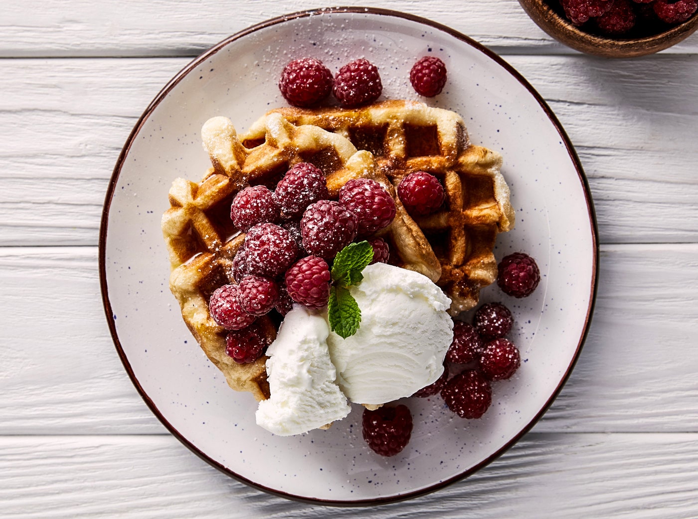 En tallerken med belgiske vafler toppet med hindbær og kugle vaniljeis.