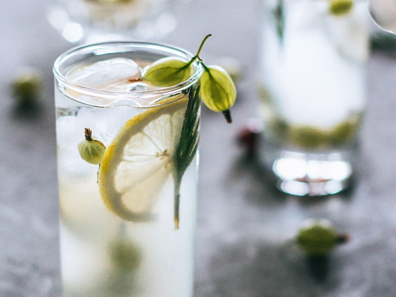 En højdrink pyntet med citron, is og en grøn bær.