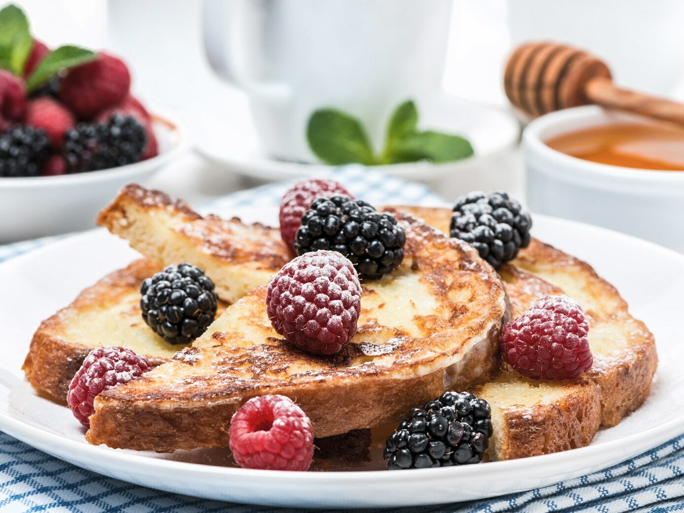 Lækker fransk toast toppet med friske hindbær og brombær på en tallerken.