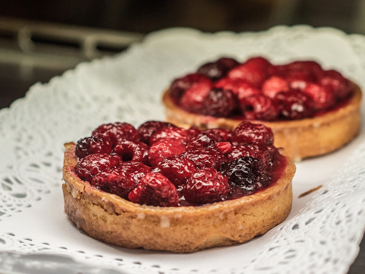 To lækre tærter toppet med røde bær på en hvid serviet