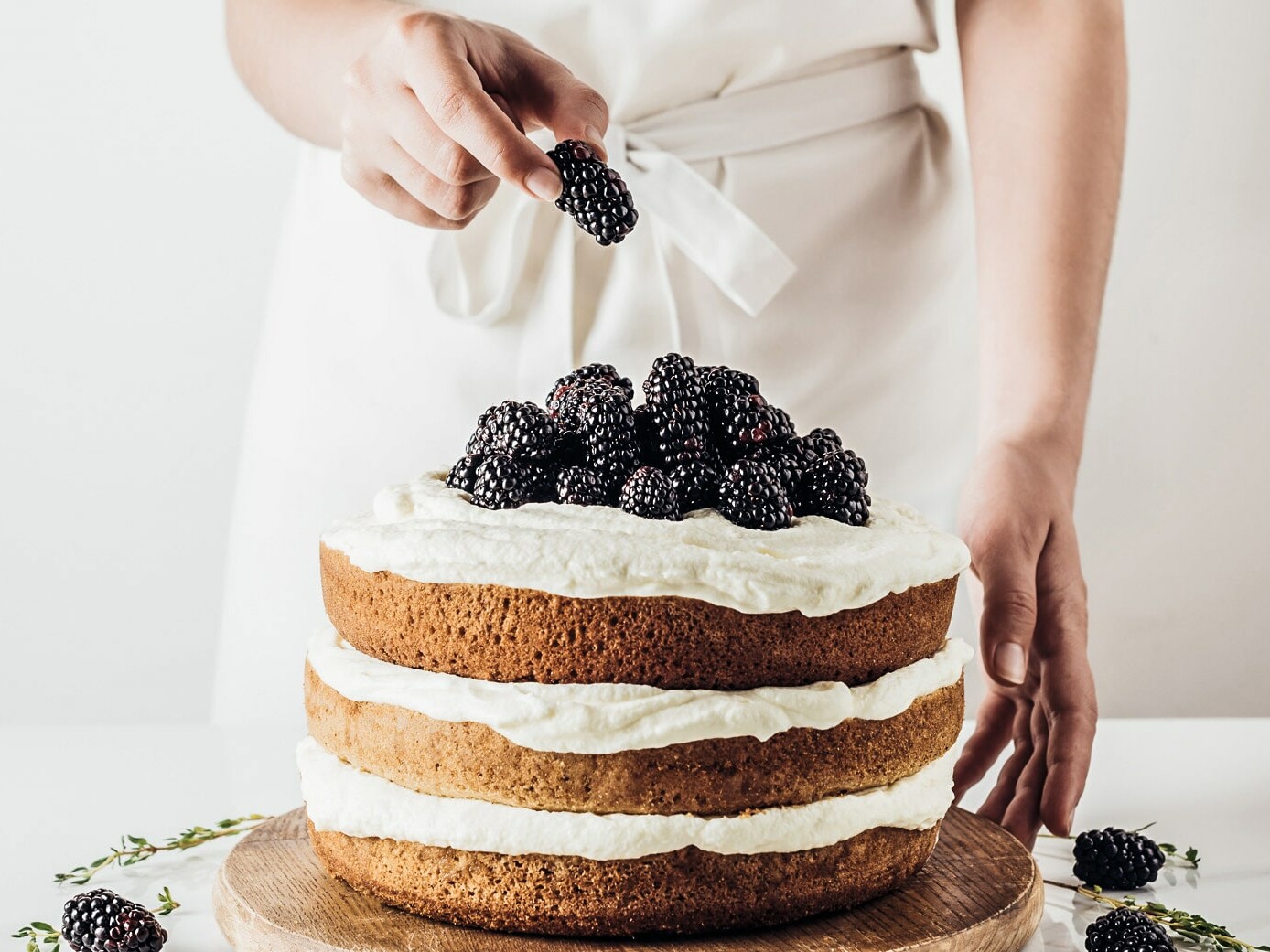 En person dekorerer en lagkage med brombær på toppen.