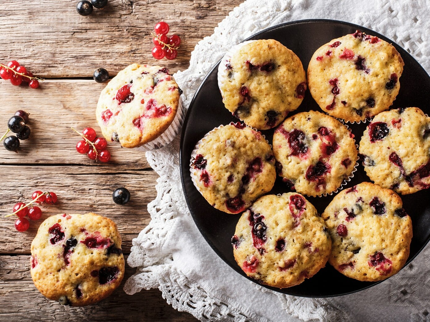 Lækre muffins med friske bær arrangeret på sort tallerken og træbord