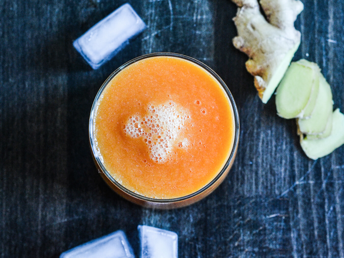 Glas med orange juice, isterninger og frisk ingefær på mørkt bord