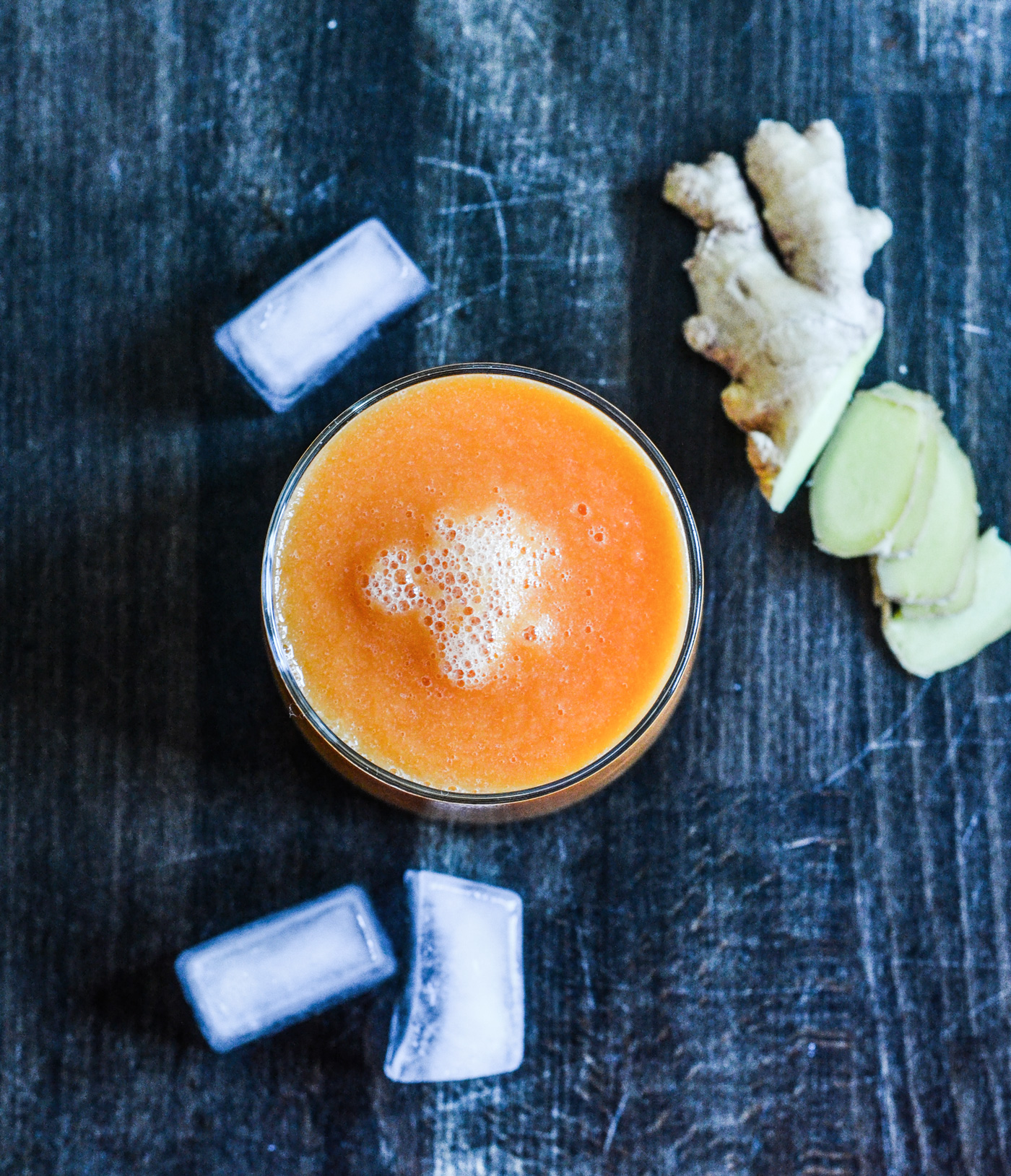 Glas med orange juice, isterninger og frisk ingefær på mørkt bord