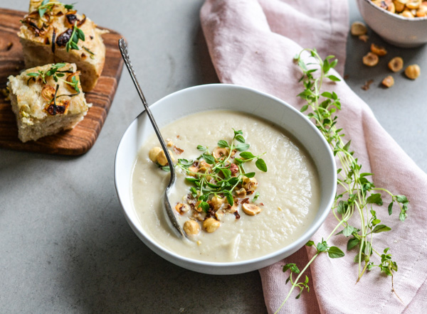En skål rodfrugtsuppe pyntet med nødder og urter, ved siden af brød
