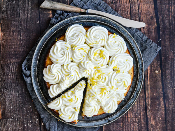 En citronkage med flødeskumstoppe på en tallerken med en skive skåret ud.