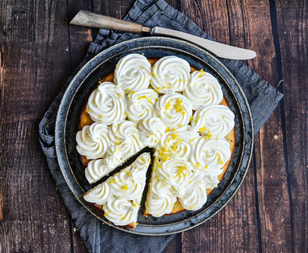 En citronkage med flødeskumstoppe på en tallerken med en skive skåret ud.