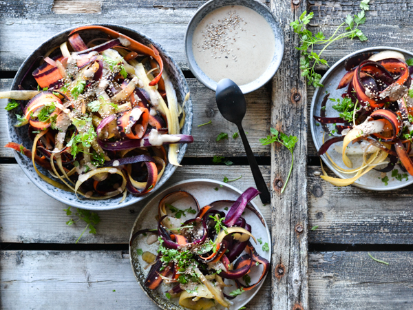 Tre tallerkener med farvet rodsalat og en skål dressing på et rustikt træbord