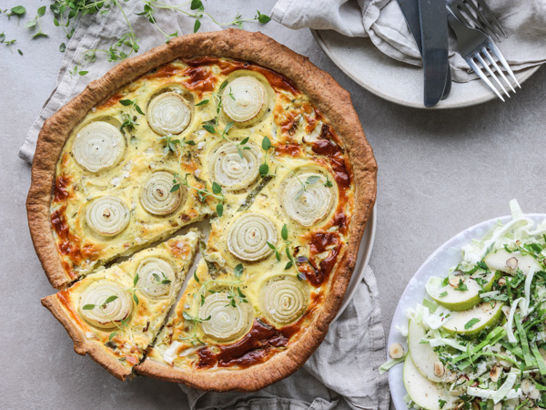 Hjemmelavet løgtærte med skiver af løg og frisk timian på toppen