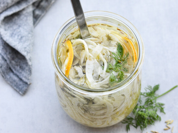 Glas med syltede grøntsager, skefuld indeni, viskestykke ved siden af