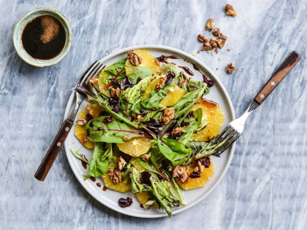 Tallerken med grøn salat, appelsinskiver og valnødder.