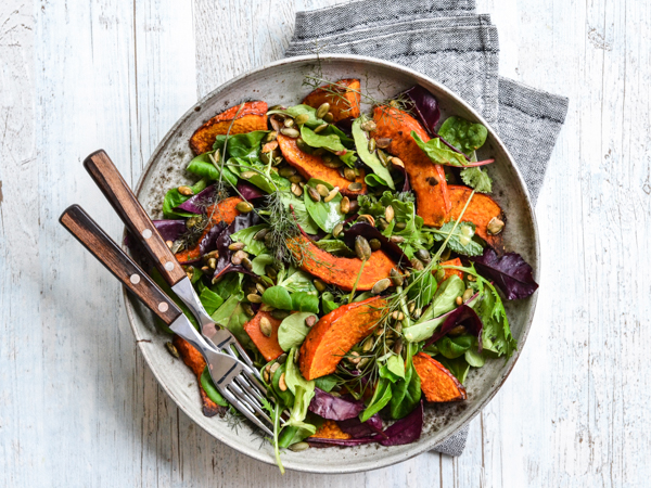 Salat med skiver af græskar, blandede blade og nødder på gråt fad