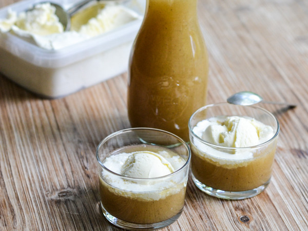 To glas med æblekompot toppet med vaniljeis og en flaske kompot ved siden af